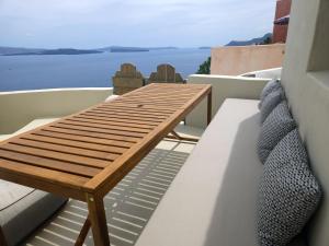 a wooden bench on a balcony with a view of the water at Phaos Oia Suites in Oia