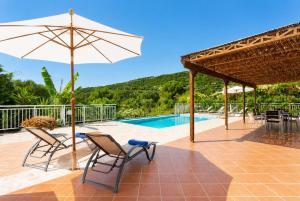 a patio with two chairs and an umbrella and a pool at Villa Peach in Katelios