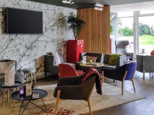 a living room with chairs and a tv on a wall at Novotel Saclay in Saclay