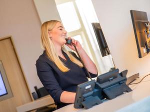 a woman talking on a phone in front of a computer at Novotel Rotterdam Brainpark in Rotterdam