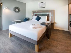 a bedroom with a large white bed with a desk at Novotel Senart Golf De Greenparc in Saint-Pierre-du-Perray