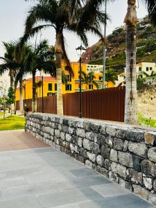 a stone retaining wall with palm trees and a yellow building at VALE MAR Guest in Ribeira Brava