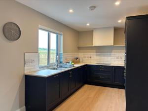 a kitchen with black cabinets and a clock on the wall at Creevy Cove cottage in Kildoney