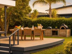 Ein Holztisch und Stühle auf einer Terrasse mit Tisch und Grill in der Unterkunft Blackpool Bayside - Stay Waiheke in Oneroa