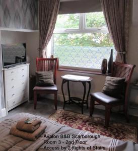a bedroom with a bed and two chairs and a window at Avalon B&B Scarborough in Scarborough