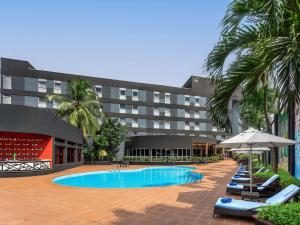 a hotel with a swimming pool with chairs and an umbrella at Novotel Port Harcourt in Port Harcourt