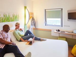 a man and a woman sitting on a couch with a laptop at ibis budget Birmingham Airport Terminal Building - NEC in Bickenhill