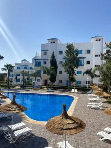 a swimming pool with chairs and umbrellas in front of a building at Cozy appartement smir park in Tétouan