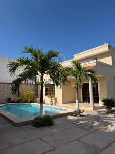 a swimming pool in front of a house with palm trees at Gated house with garden and pool Mérida in Caucel