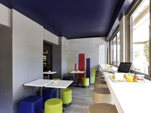 a restaurant with white tables and colorful stools at IBIS Budget Aix en Provence Est Le Canet in Meyreuil