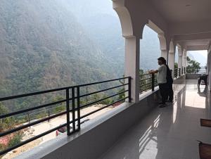 a man standing on a balcony looking out at the mountains at Panchkedar resort in Sonprayag
