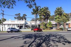 a red car driving down a street with palm trees at Tocumwal Hotel Motel in Tocumwal