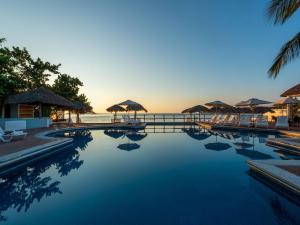 a swimming pool with chairs and umbrellas and the ocean at Park Royal Beach Huatulco in Tangolunda
