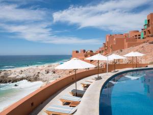 a swimming pool with chairs and umbrellas next to the ocean at Club Regina Los Cabos in San José del Cabo