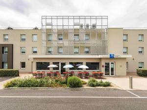 a building with tables and umbrellas in front of it at ibis budget Saint Pourcain in Saint-Pourçain-sur-Sioule