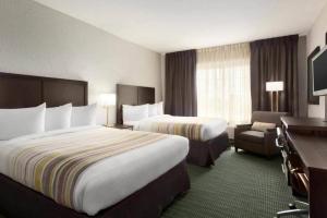 a hotel room with two beds and a chair at Hotel Flamingo Inn & Suites Vero Beach I-95 in Vero Beach