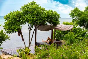 a woman sitting in a chair under an umbrella near the water at Kizikula - Boutique Hotel in Kizimkazi