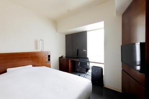 a bedroom with a bed and a desk and a television at JR Inn Sapporo in Sapporo