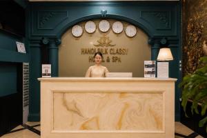 a woman standing behind a counter in a room with clocks at Hanoi Silk Classy Hotel & Travel in Hanoi