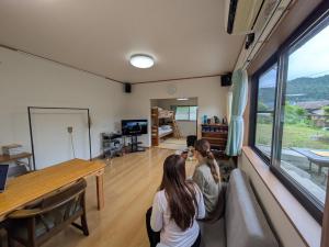 two women sitting on a couch in a room with a large window at 平屋宿まえの in Motoyama