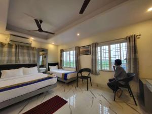 a bedroom with two beds and a person sitting in a chair at Hotel Shreesh Mayapur in mayapur