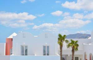 a white building with palm trees in the foreground at New Haroula in Fira