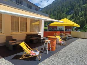 a patio with chairs and tables and a yellow umbrella at Pension Edelweiss - Bergdorf Gargellen 1423m - 200m zur Schafbergbahn in Gargellen