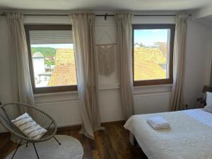 a bedroom with a bed and a chair and two windows at Daddy's home in Hargesheim