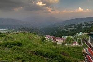 a view of a green hill with mountains in the background at The Cedar Valley l Restaurant and Cafe l Forest Treks l Kufri by Exotic Stays in Shimla