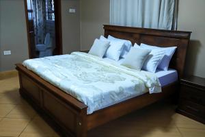 a large bed with white sheets and pillows at Kingram Apartments in Entebbe