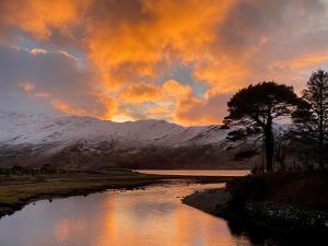 a sunset over a river with snow covered mountains at Corran Shepherds Hut in Corran