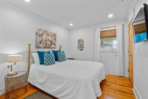 a white bedroom with a large bed with blue pillows at Downtown Fairhope Cottage in Fairhope