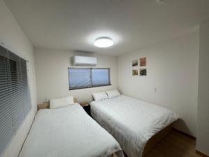 two beds in a small room with a window at 羽憩館 Hakeikan KIX in Izumi-Sano