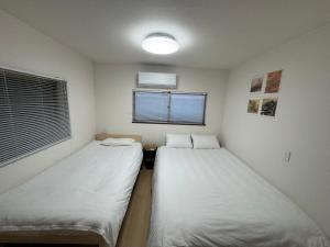 two beds in a small room with a window at 羽憩館 Hakeikan KIX in Izumi-Sano