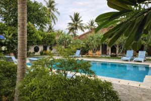 a resort pool with chairs and palm trees at GGuesthouse in Kuta Lombok