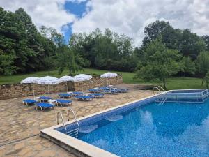 a pool with chairs and umbrellas next to a stone wall at Къща Цачеви in Tryavna