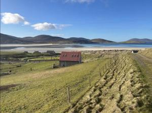 a barn in a field next to a body of water at Harris Cuckoo Cottage in Luskentyre