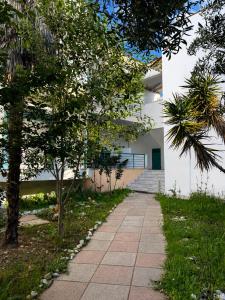 a sidewalk in front of a white building with trees at Pefkostalia in Pefkochori