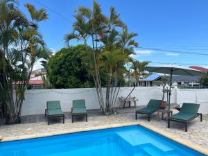 a pool with chairs and an umbrella and palm trees at Coco Banana in Baie-Mahault