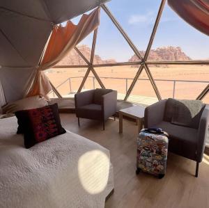 a room with a bed and chairs and a view of the desert at Ain Rum Luxury Camp in Wadi Rum