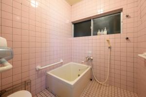 a bathroom with a tub and a toilet and pink tiles at yadobankkukomae19 in Fukuoka