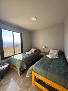 two beds in a room with a large window at El Tesoro de Yacanto in Villa Yacanto