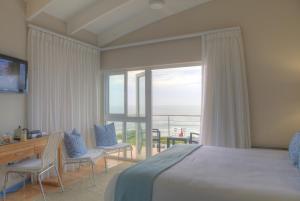 a bedroom with a bed and a desk and a balcony at Periwinkle Lodge Guest House in Plettenberg Bay +43 photos