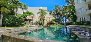 a swimming pool with two chairs and umbrellas next to a building at Seaside 3 suites Penthouse with Pool Gym & BBQ Terrace in Cap Malheureux