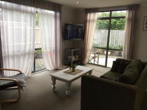 a living room with a couch and a table and windows at Relaxing Beach Side House in Porirua