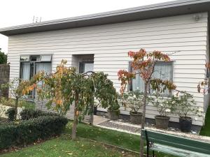 a house with trees in front of it with a bench at Relaxing Beach Side House in Porirua