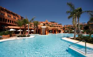 a swimming pool in a resort with palm trees and buildings at Royal Hideaway Sancti Petri in Chiclana de la Frontera