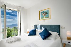 a white bed with blue pillows and a window at Gocce Di Capri Resort in Massa Lubrense