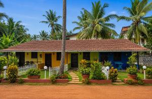 a yellow and blue house with palm trees in the background at Vinsons Cottages in Colva