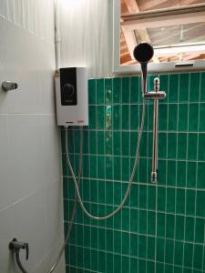 a shower with a hose attached to a green tiled wall at Tamarind nest in Sai Yok